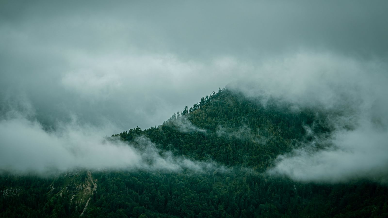 A far out view of a mountain with clouds covering the mountain.