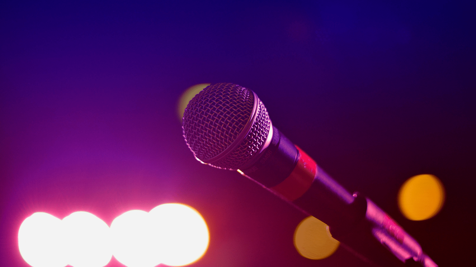 Microphone on a stand against a blurred stage with bright lights, hinting at a performance.