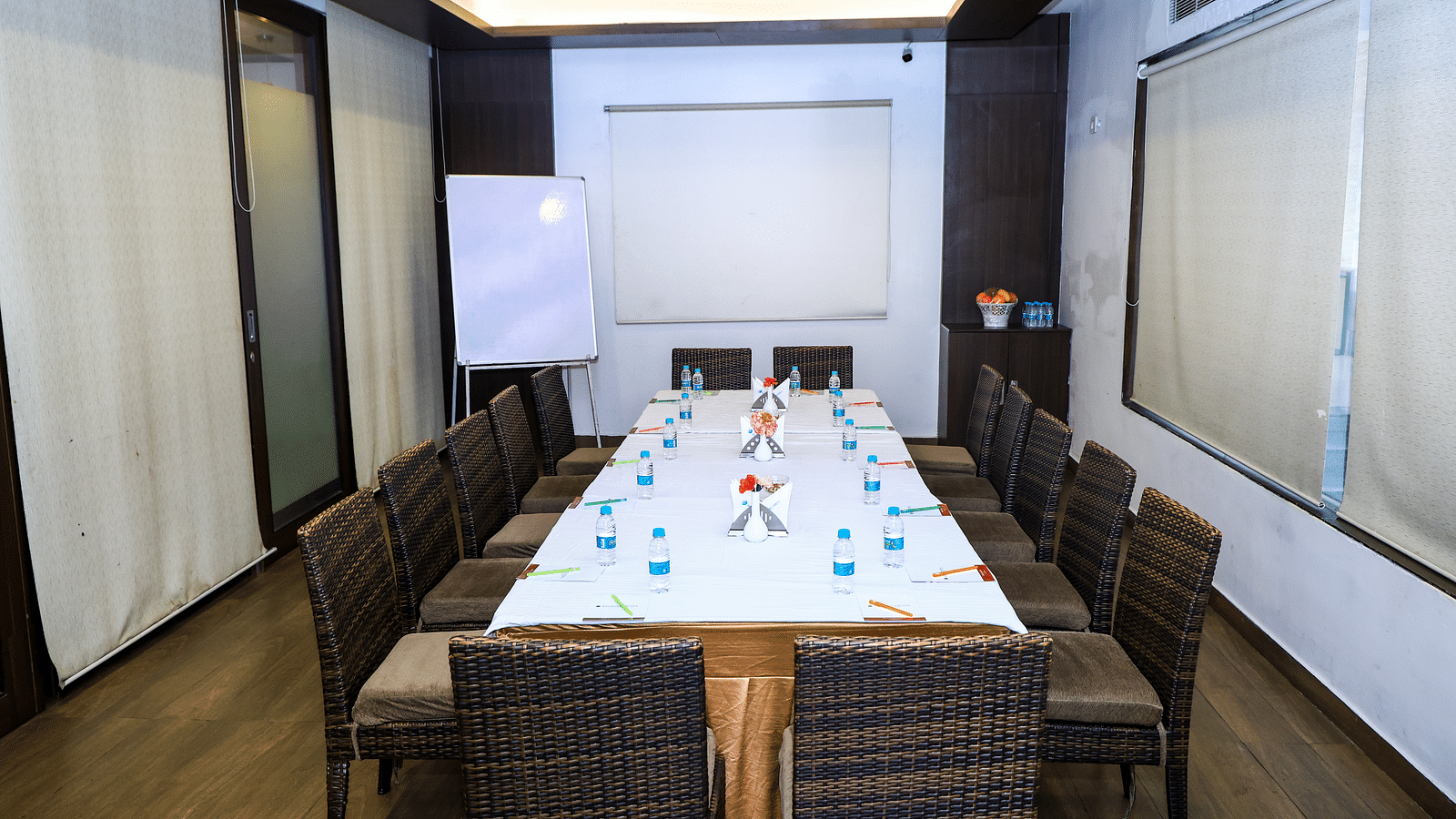A modern, well-lit meeting room with a long rectangular table, chairs, a whiteboard, and large windows Cotio - The Boardroom at Khanna Fiesta