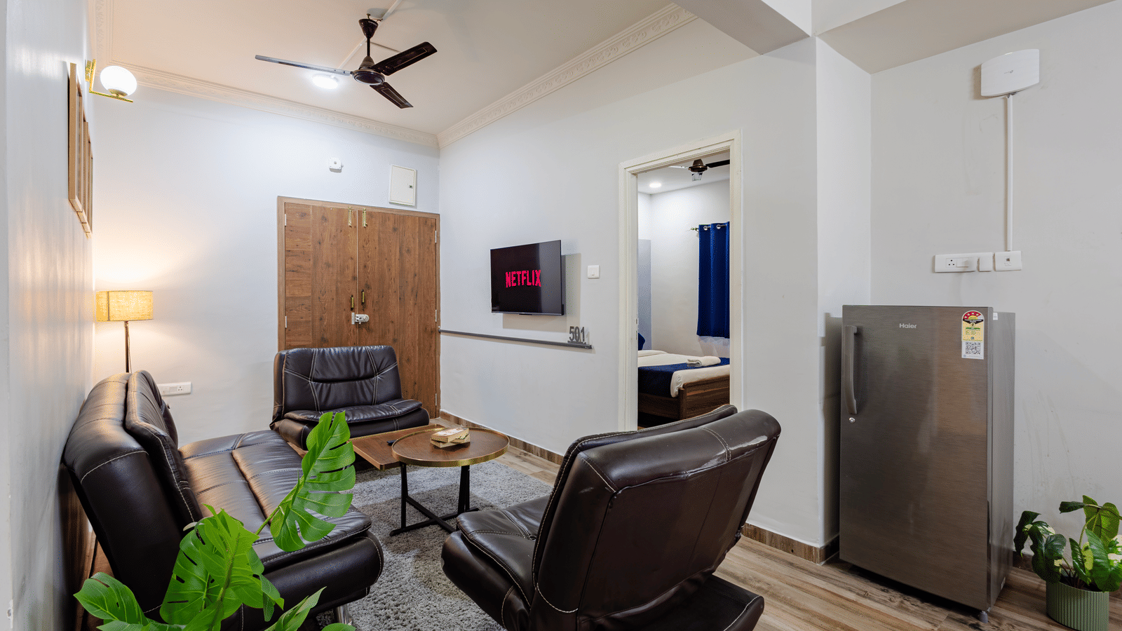 Separate living room of 4BHK featuring sofas with a centre table facing the wall-mounted TV and a doorway leading to an inner bedroom.