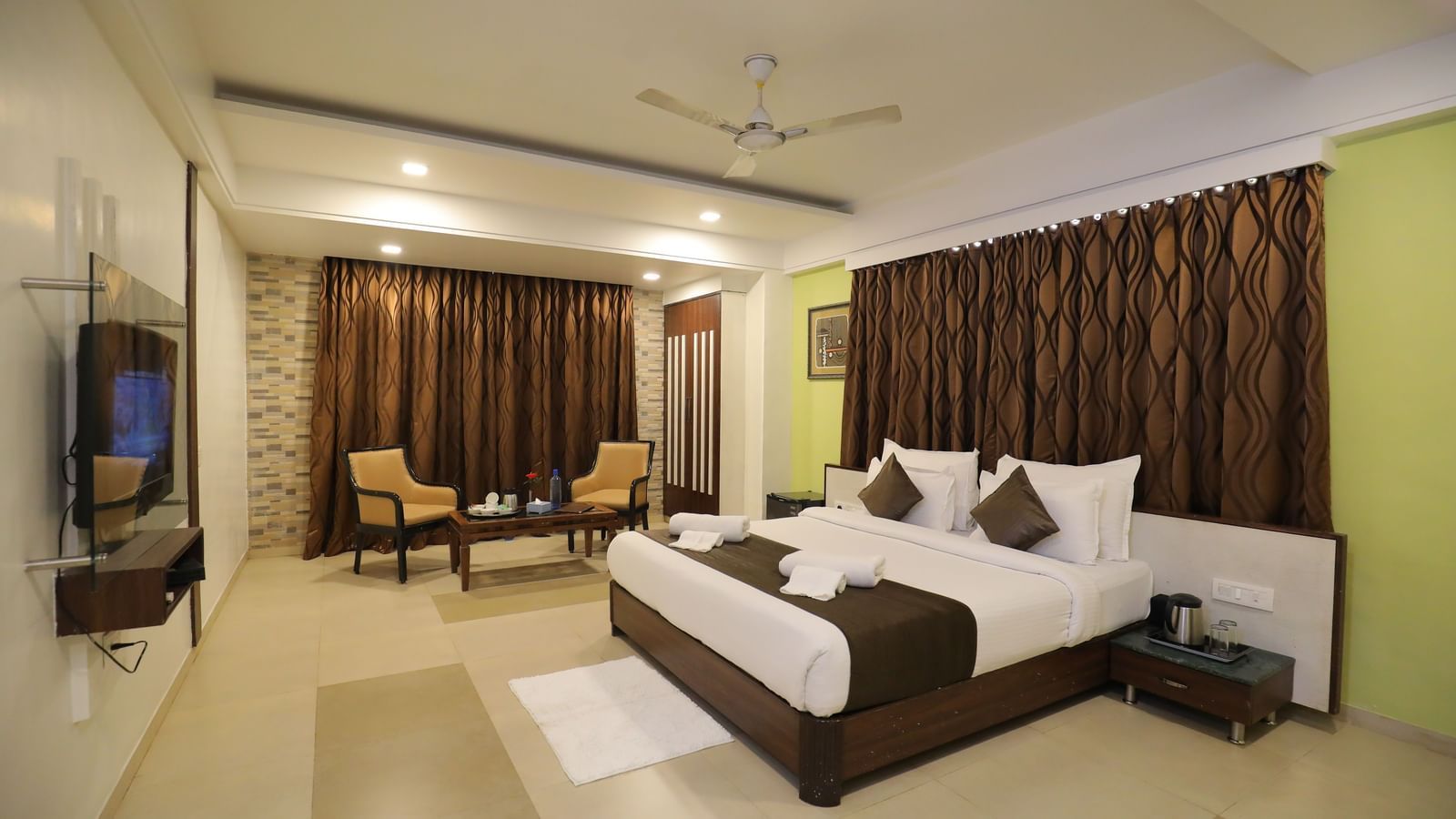 A spacious bedroom at Krushnai Resort featuring a king size bed, wall-mounted TV, and brown drapes.