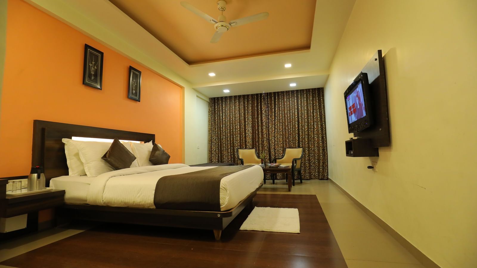 A spacious bedroom at Krushnai Resort with a bed, an orange wall, and a large TV mounted on the wall.