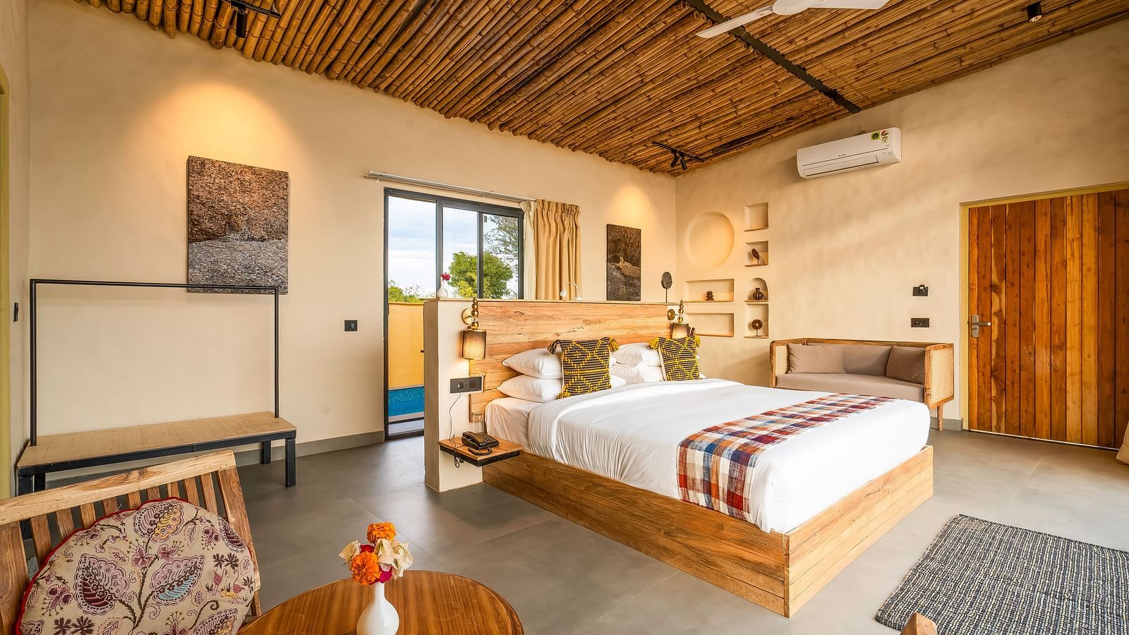 An image of a wooden furnished bedroom  featuring a double size bed, a  chair and centre table, a sofa, AC, fan,  and some decorative items - Kurja Jawai