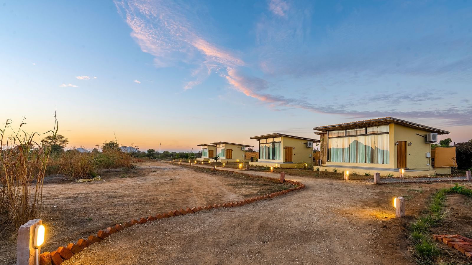 An image of cottages at Kurja Jawai with a huge lawn and some plants and an open sky behind 