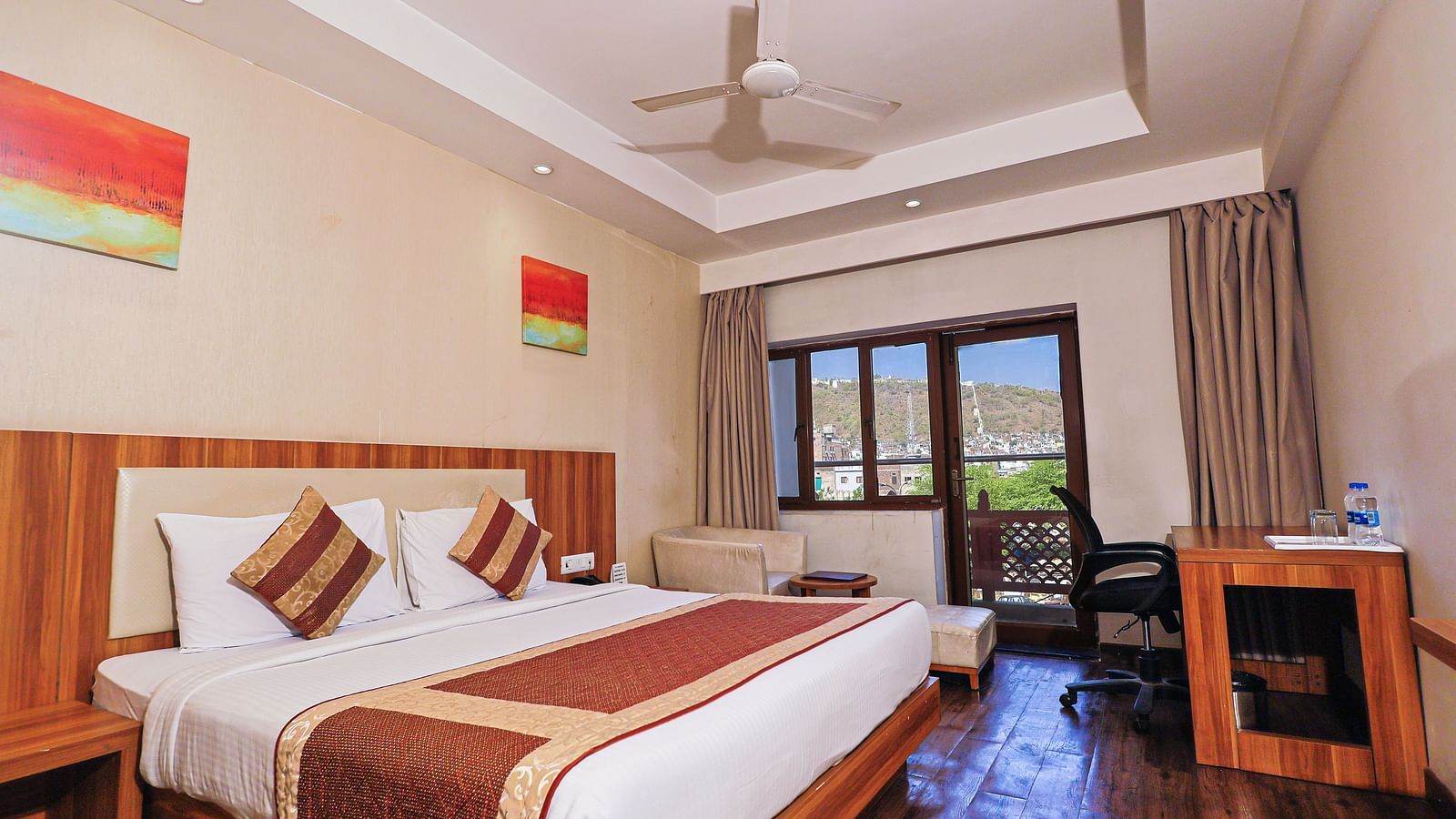 A low angle view of the bedroom with comfy bed and balcony, table and fan at Le Roi Udaipur