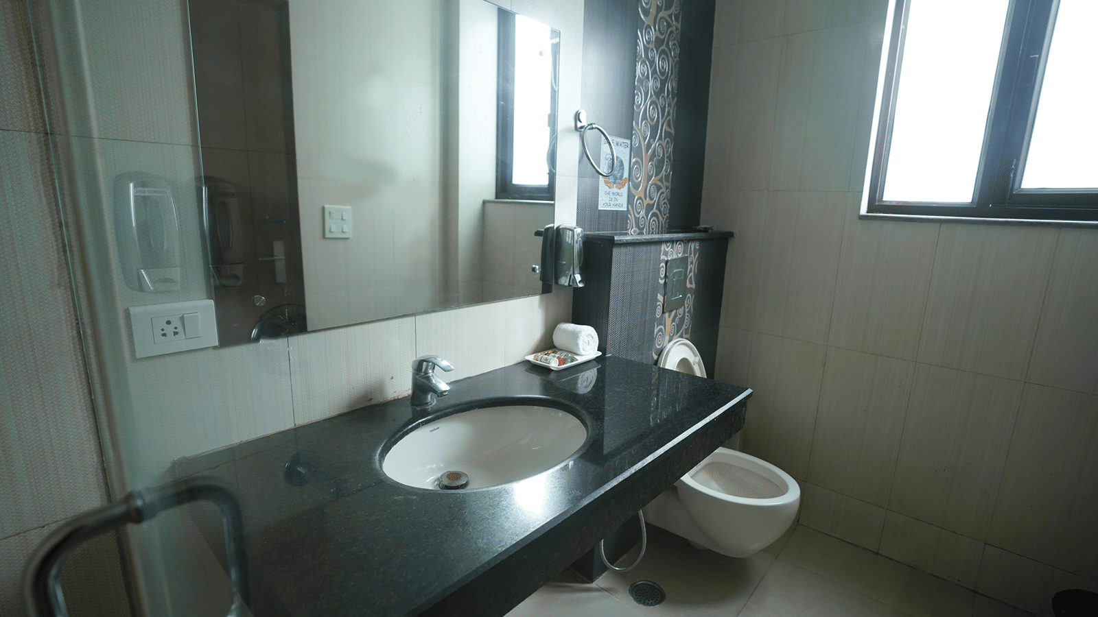 Bathroom with a granite vanity, sink, mirror, a rolled towel, a wall-hung toilet and a frosted window.