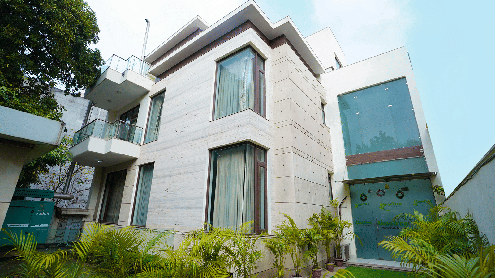 Entrance with a stone facade, branded glass doors with wreaths, potted areca palms and artificial grass.