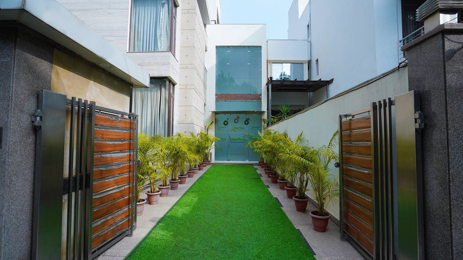 Hotel entrance with a landscaped walkway, manicured greenery and secure gates.
