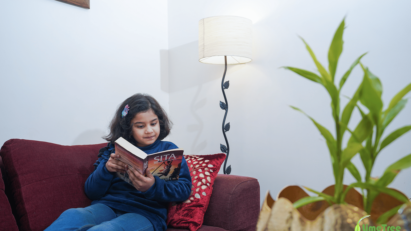 Child reading the book SITA on a maroon sofa in the seating corner of Lime Tree Hotel Near 32nd Avenue.