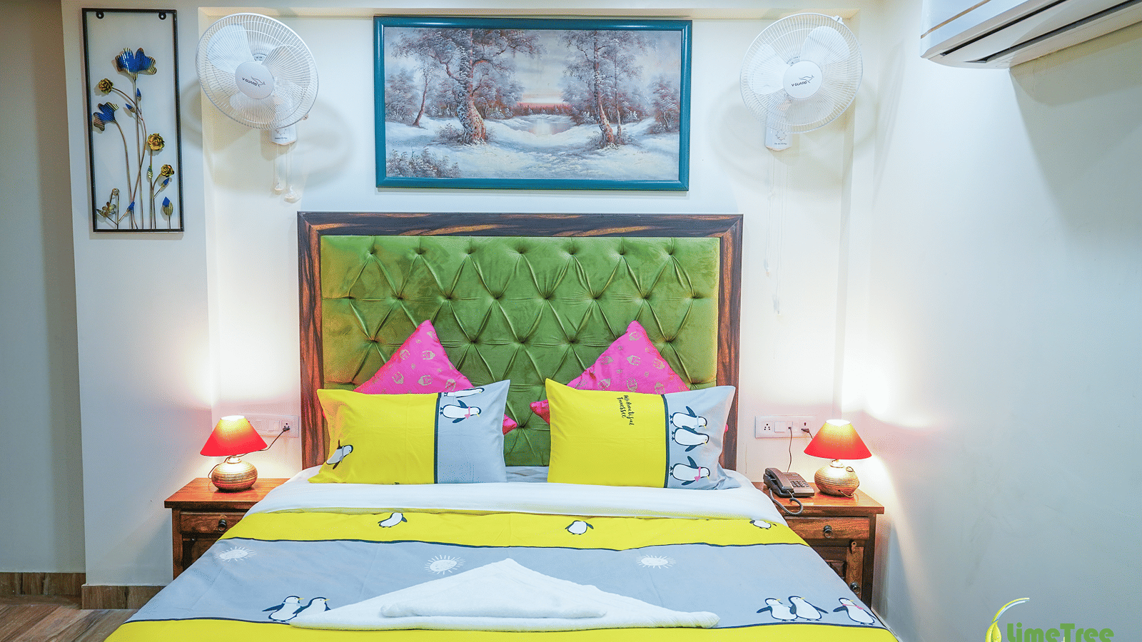 Bedroom at Lime Tree Hotel Near 32nd Avenue with a green tufted headboard, a snowy forest painting and red table lamps.