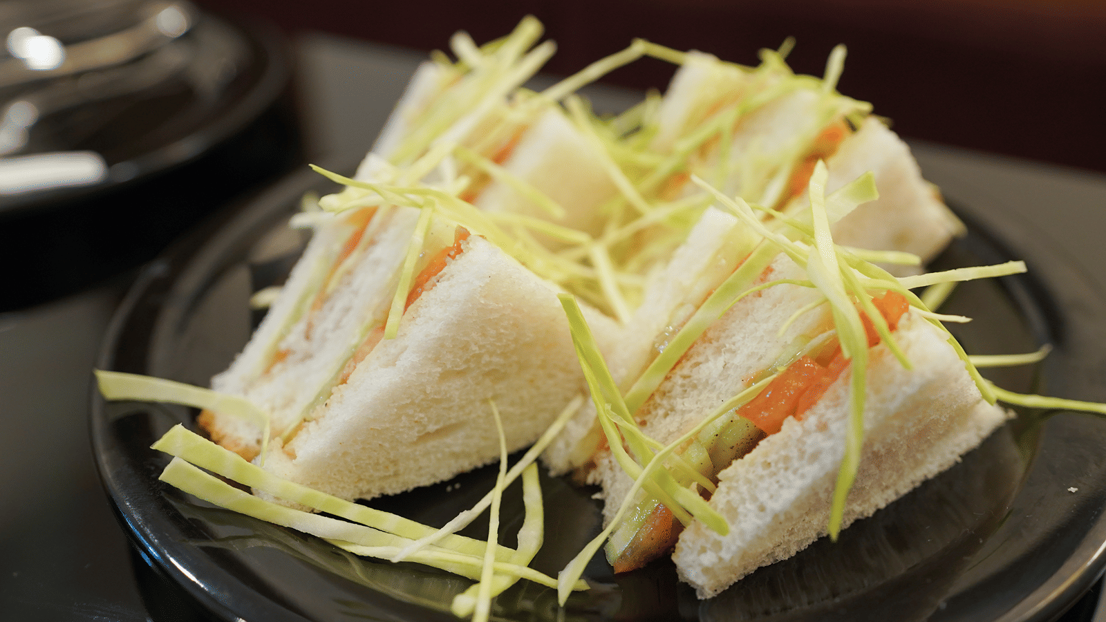 Grilled vegetable sandwich cut into triangles, topped with shredded cabbage, on a black plate.