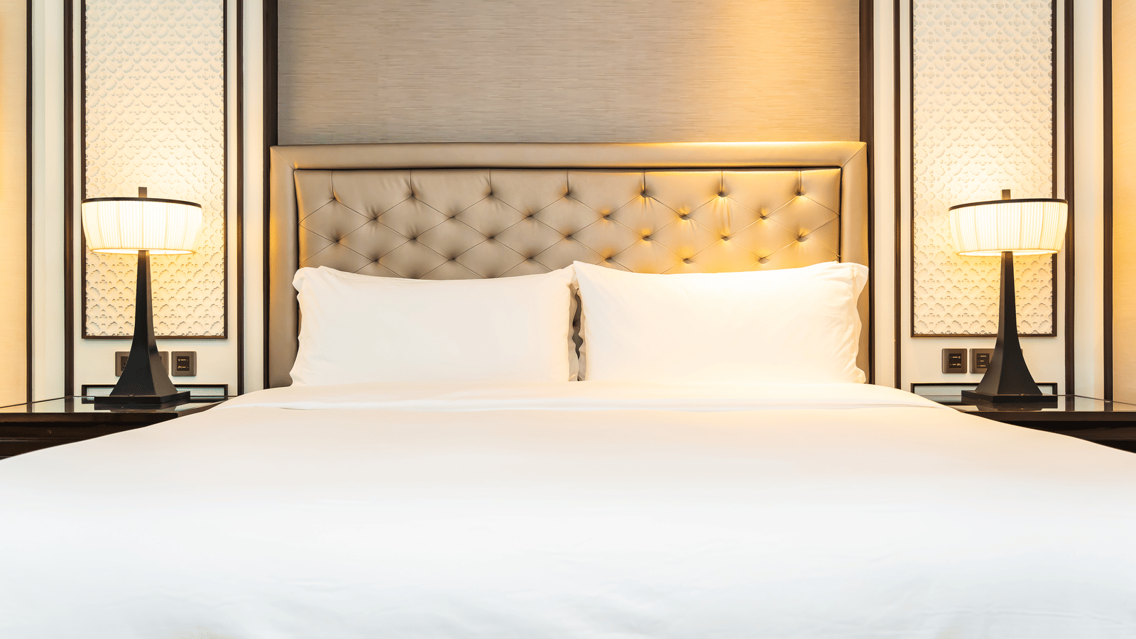 A bedroom showcasing a double bed with a tufted headboard with matching lamps and bedside tables.