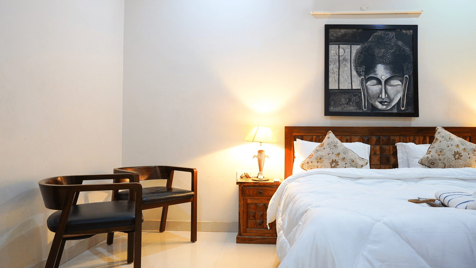 Bedroom of Lime Tree Hotels & Service Apartment Private Limited featuring a wooden bench, a padded headboard, and framed wall art.