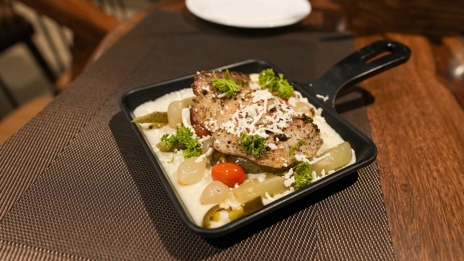 Side view of creamy pasta with grilled chicken and vegetables in a black skillet on a table at TGI Livancia Hillside, JC Nagar, Mysore