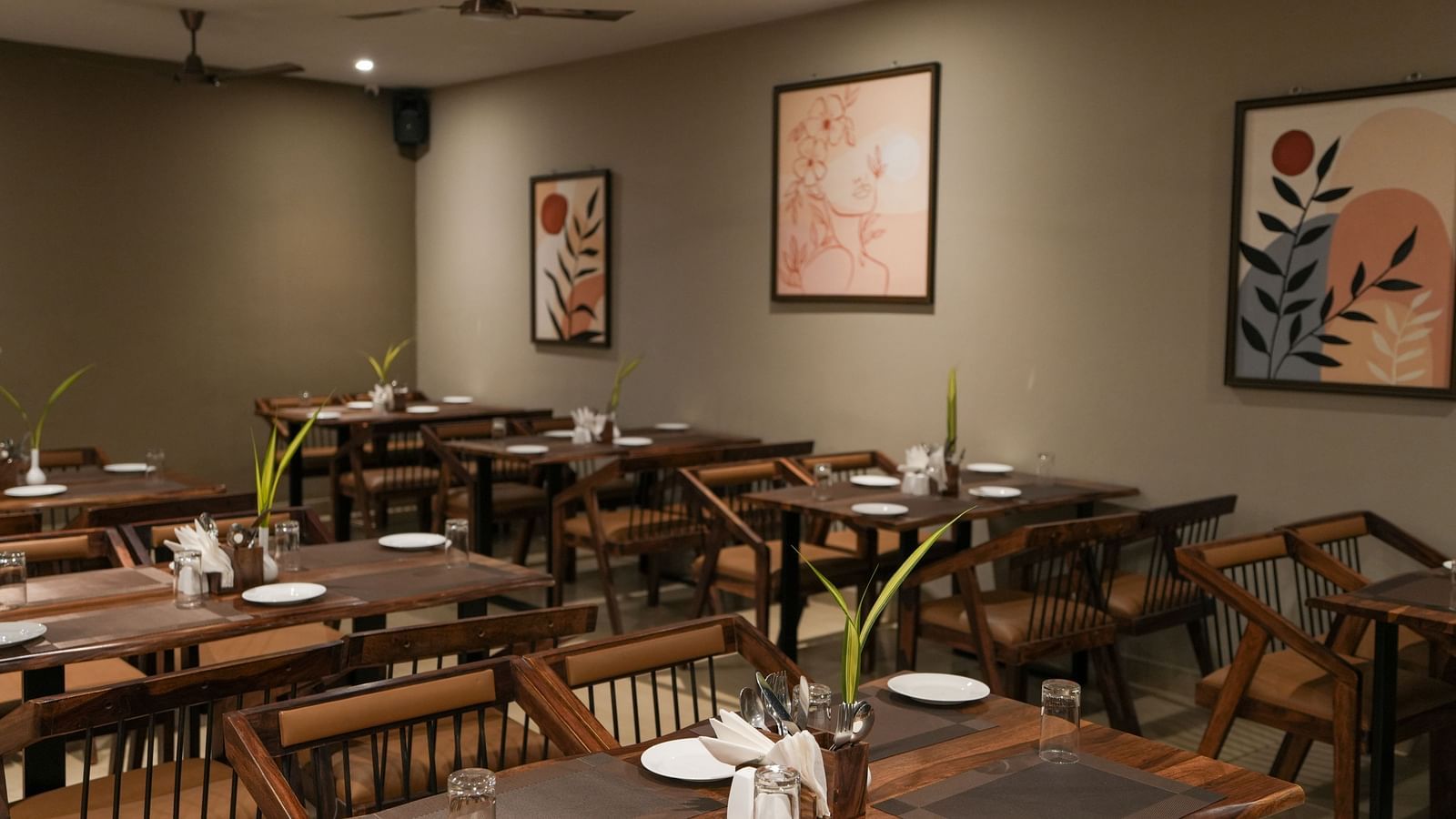 Multiple wooden tables and chairs with simple decor and botanical artwork on the wall at TGI Livancia Hillside, JC Nagar, Mysore