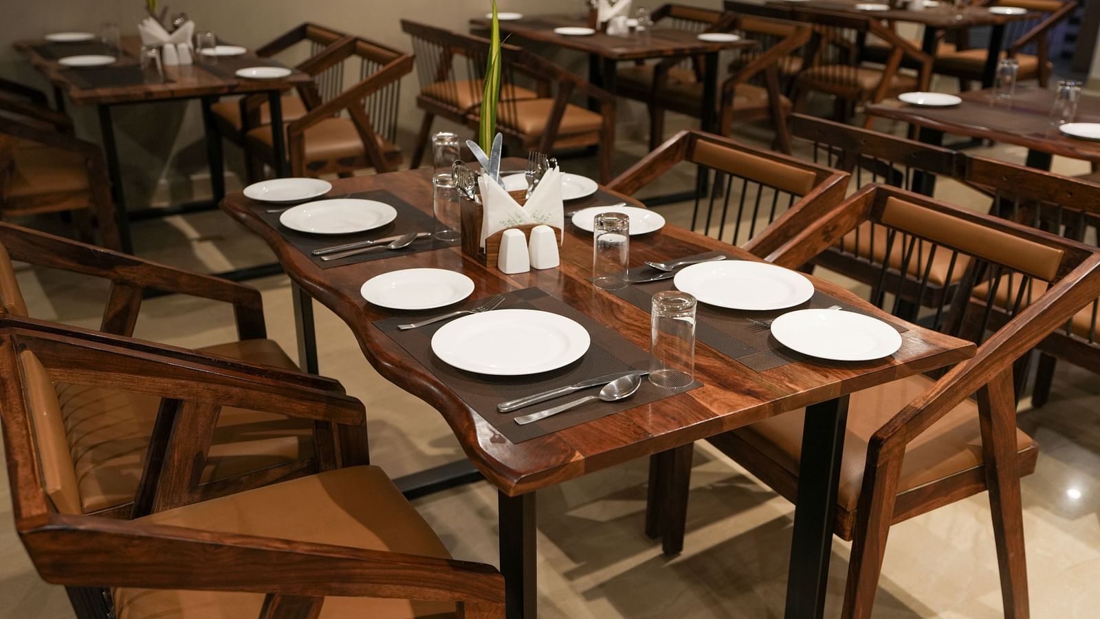Close-up of a wooden table set for six with curved edges and modern wooden chairs at TGI Livancia Hillside, JC Nagar, Mysore