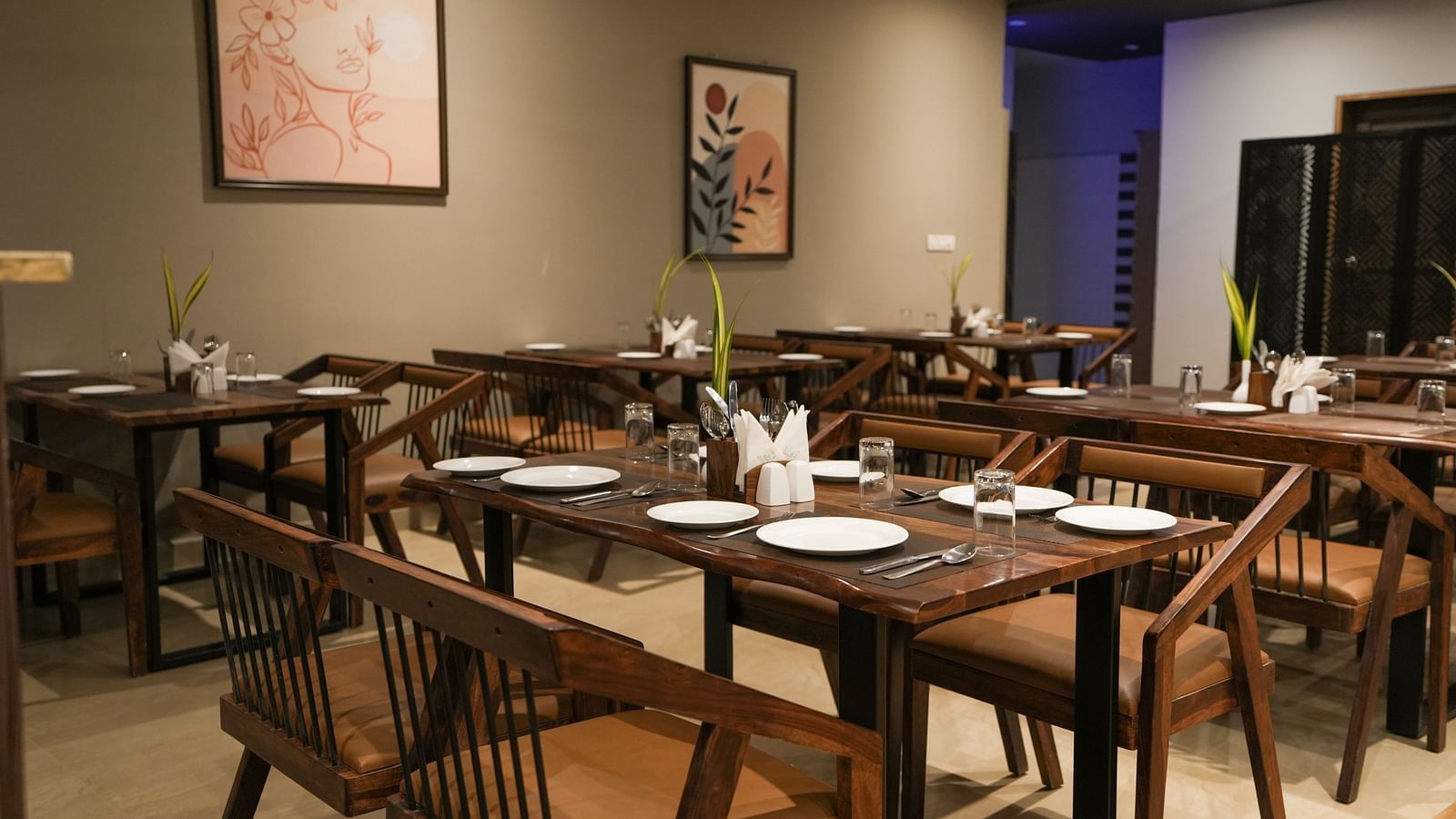 Wooden dining tables set with white plates, glasses, and cutlery in a warmly lit restaurant at TGI Livancia Hillside, JC Nagar, Mysore