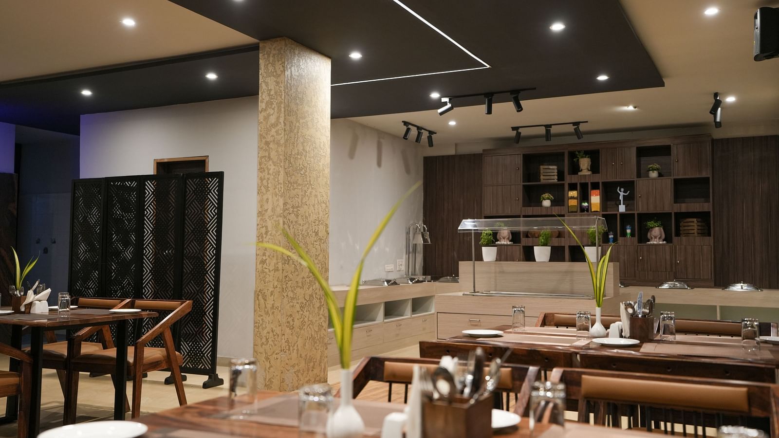 Dining area facing the buffet counter with decorative lighting and modern wooden furniture at TGI Livancia Hillside, JC Nagar, Mysore