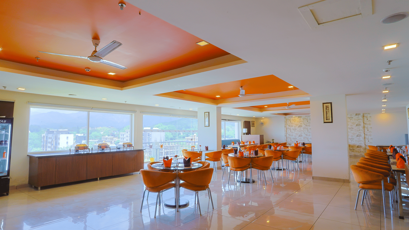 A wide view of Cafe Treat at Livbox, Dehradun, showcasing a view of the surroundings through glass windows, a spacious interior with dining tables.