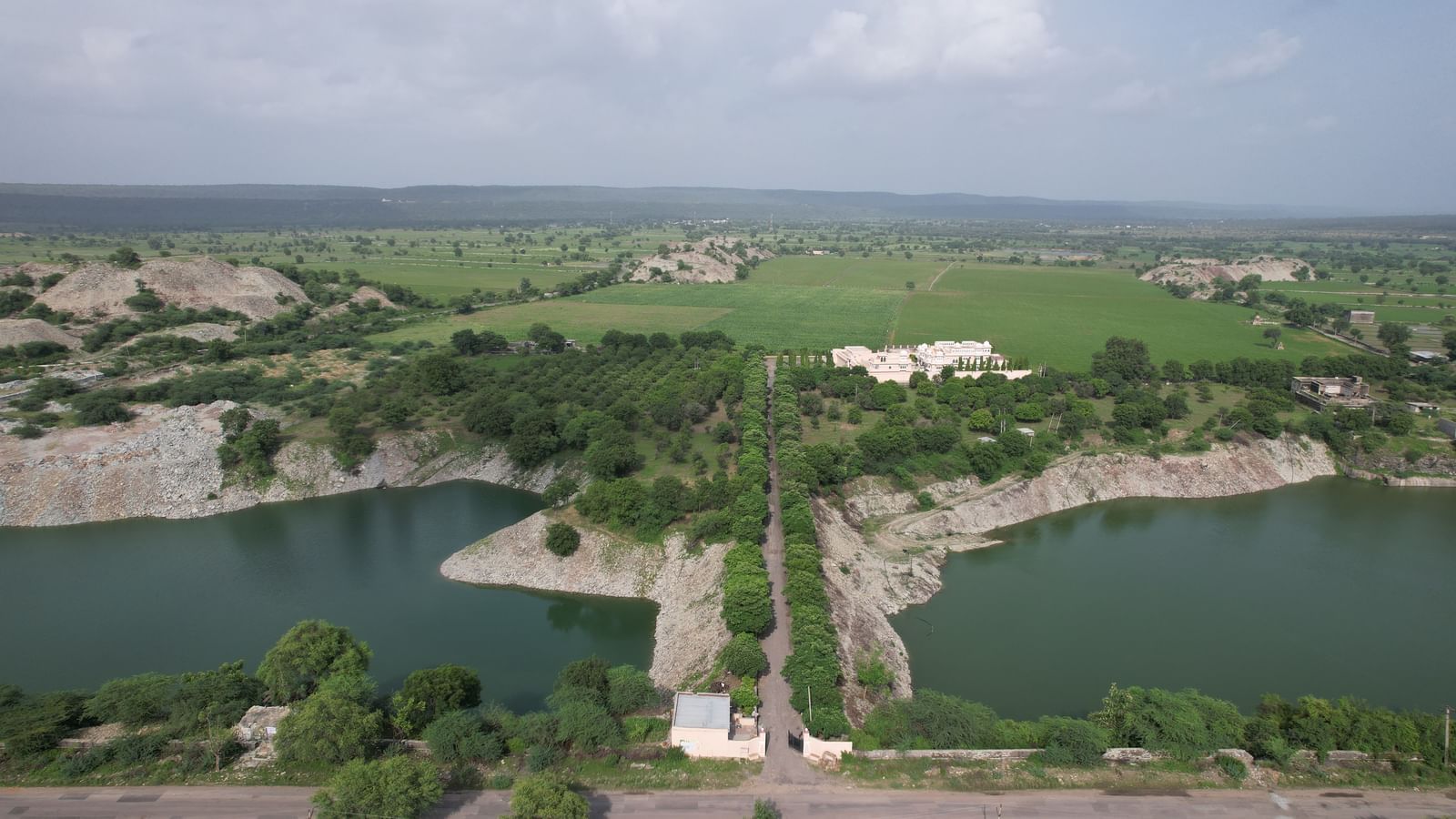 An expansive aerial view of Mahendra Niwas, nestled amidst verdant fields and a serene lake, capturing the grandeur of the estate within its natural landscape.