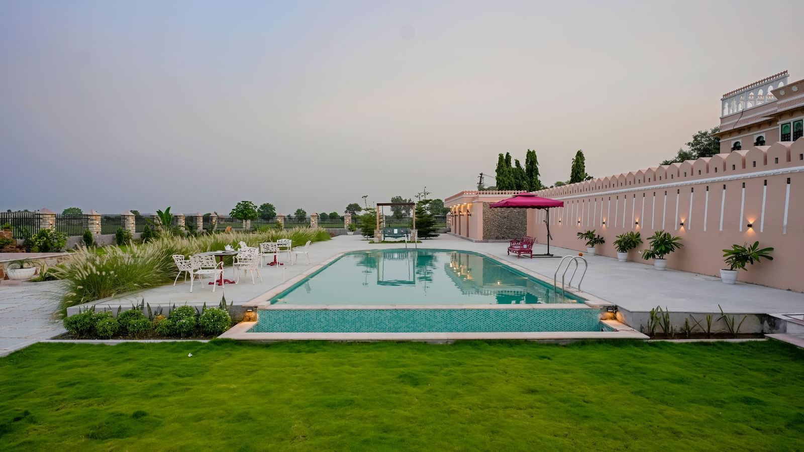 An eye-level shot of Mahendra Niwas, showcasing its luxurious swimming pool and well-maintained gardens under a soft, overcast sky.