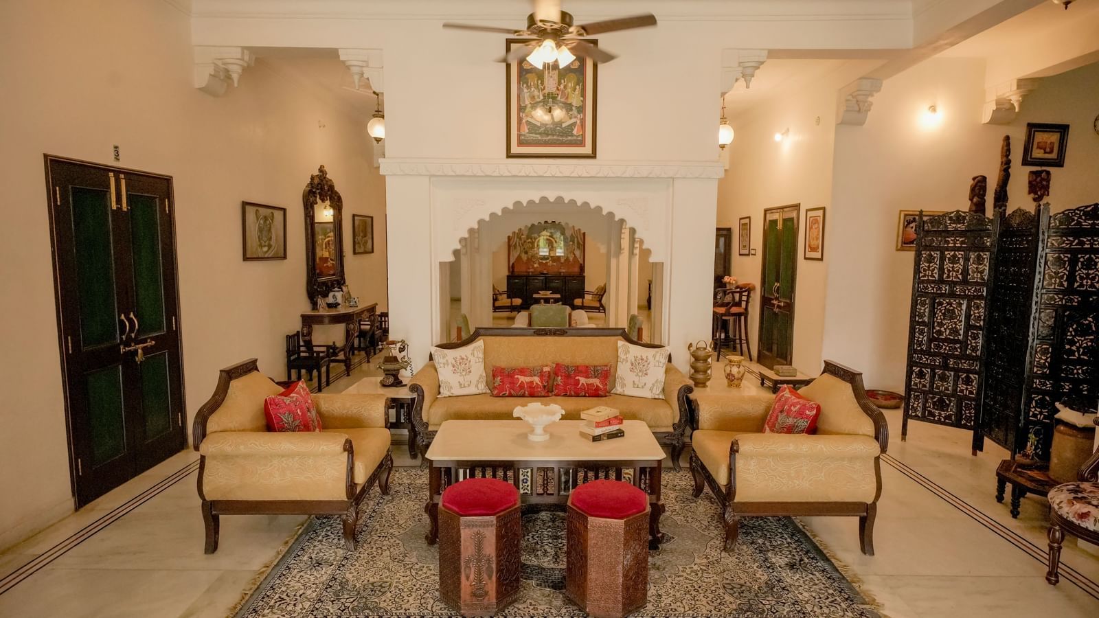  A cozy and elegant drawing-room in Mahendra Niwas, featuring twin-cushioned sofas, a central coffee table, and red ottomans.