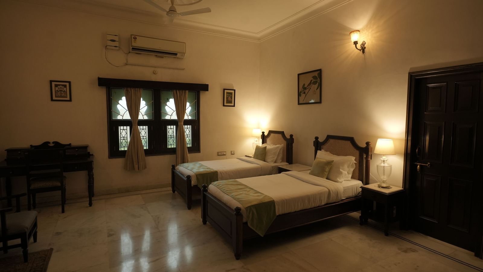  A well-lit twin room at Mahendra Niwas featuring two single beds with green and white bedding, a desk, and traditional decor.