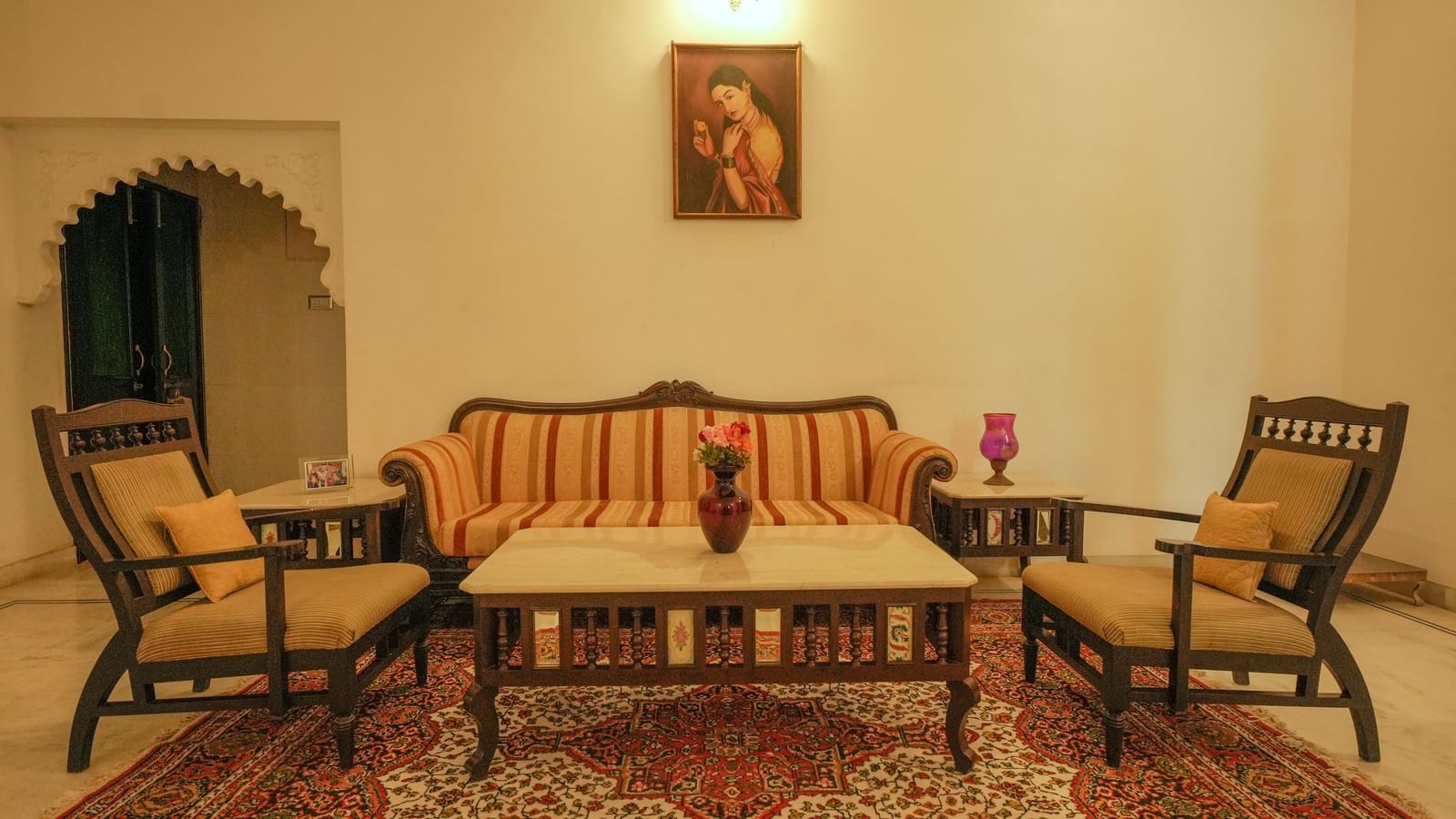 A stylish sitting area in the Terrace Orchard Suite at Mahendra Niwas. The room features a striped sofa facing two chairs, with a low table in the center and a small side table.