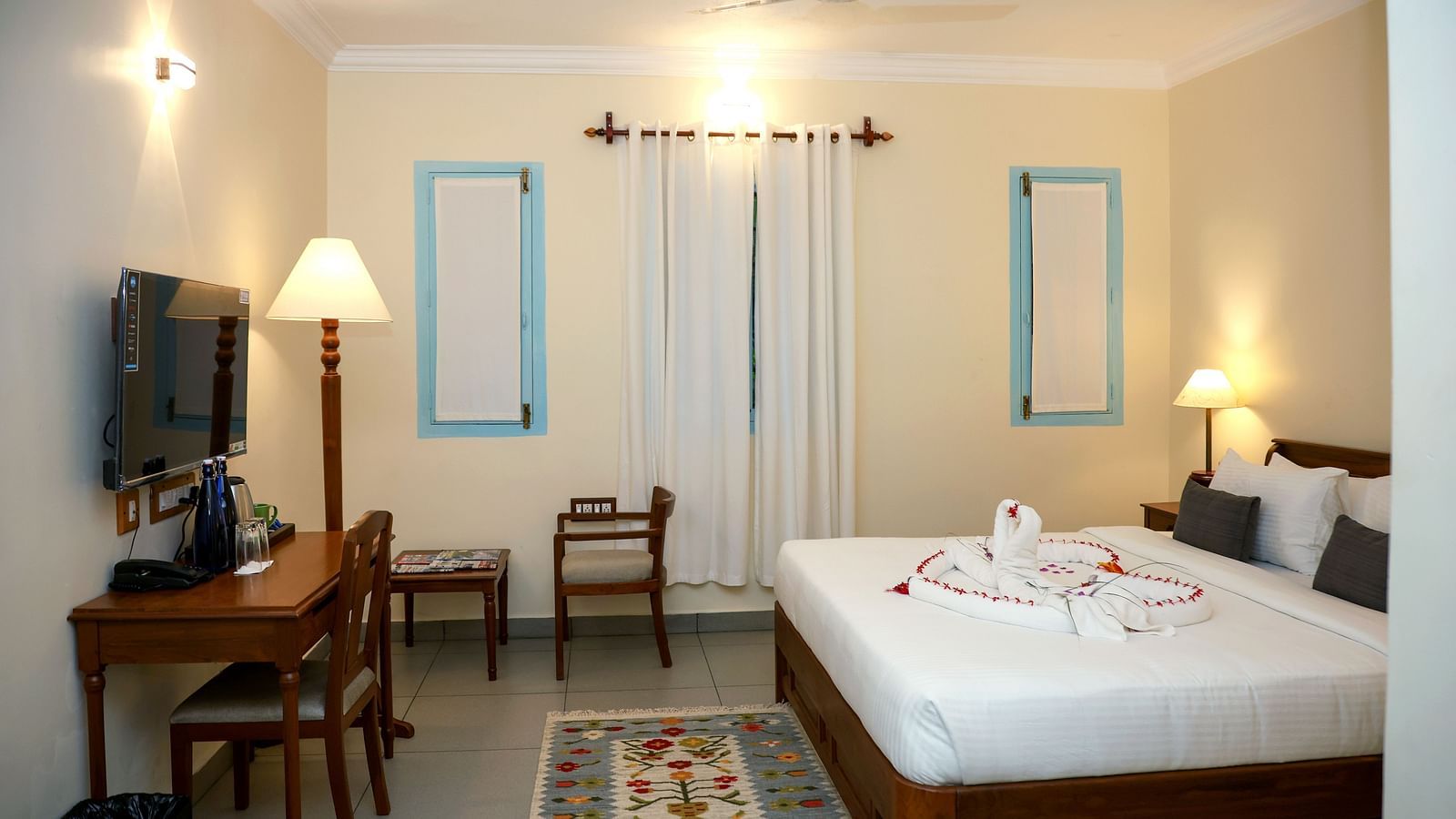 A suite with a large bed, flat screen TV, table and chair, and three lamps of different sizes | Mango Hill La Serene, Pondicherry