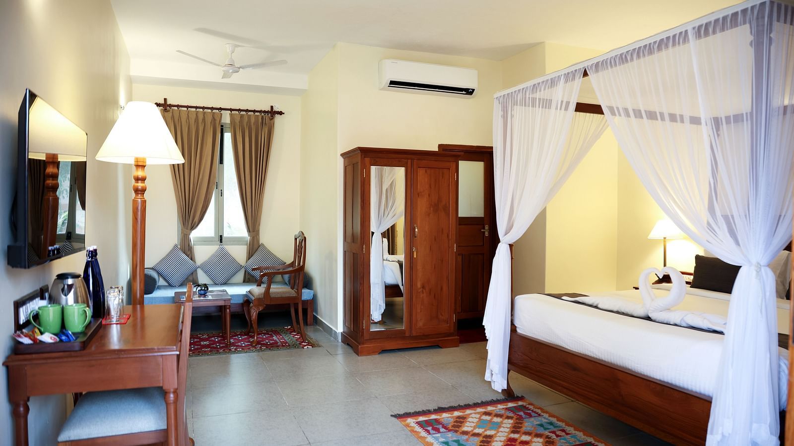 A room that has a poster-bed, a cupoard, sitting area, table and chair, etc.A sitting area, a cupboard, and a tall lamp | Mango Hill La Serene, Pondicherry
