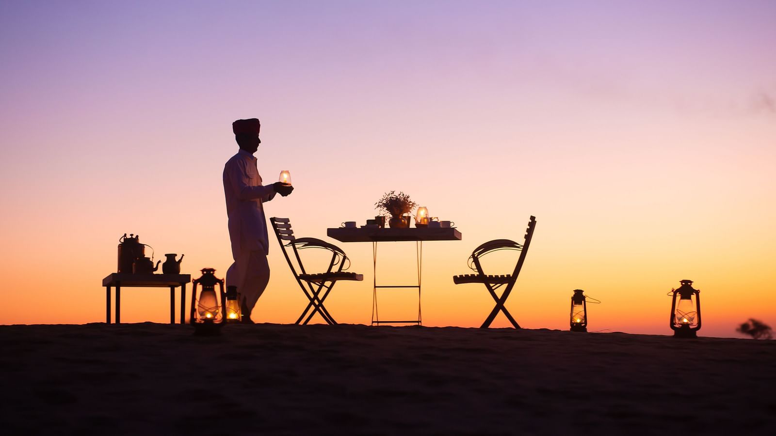 A man with a table a table and a chair in a sunset view - MANVAR Resort & Desert Camp