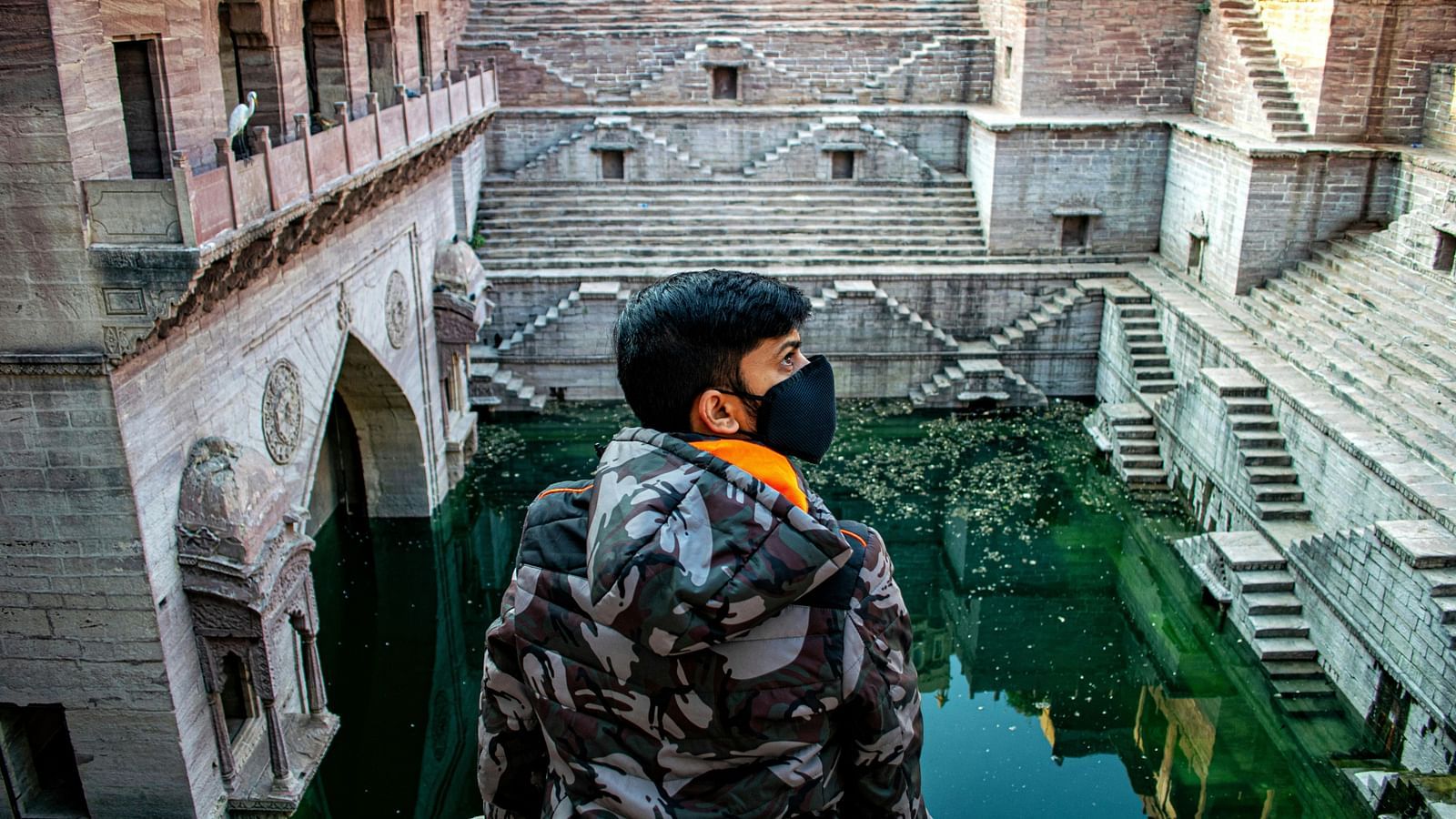 image of a man sitting on the corner brink of Toorji ka jhalra bavdi in jodhpur with green crystal clear waters