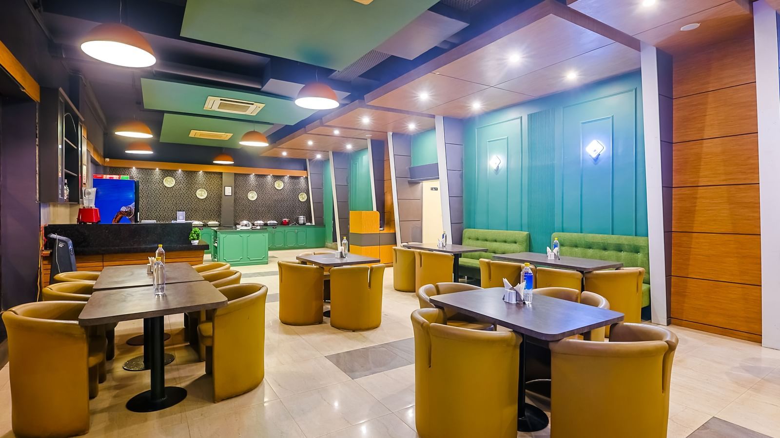 Restaurant dining area with round tables, cushioned chairs and lighting at Max Hotel Prayagraj.