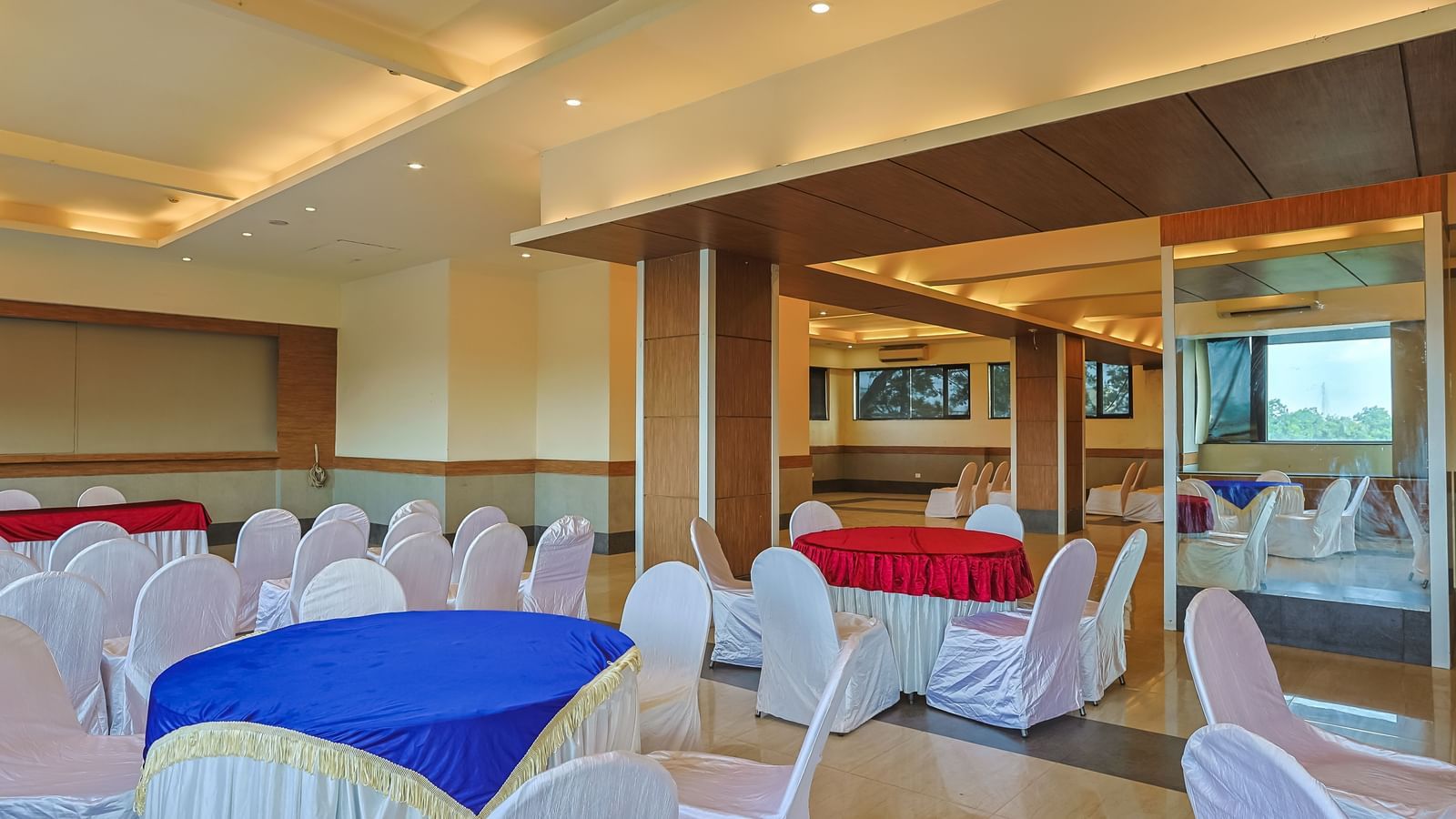 Banquet hall with round tables, white chairs and warm lighting at Max Hotel Prayagraj.