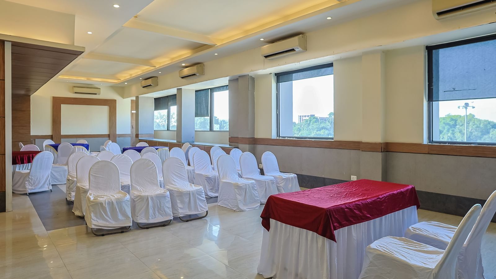 Banquet hall with rectangular tables, white chairs and large windows at Max Hotel Prayagraj.