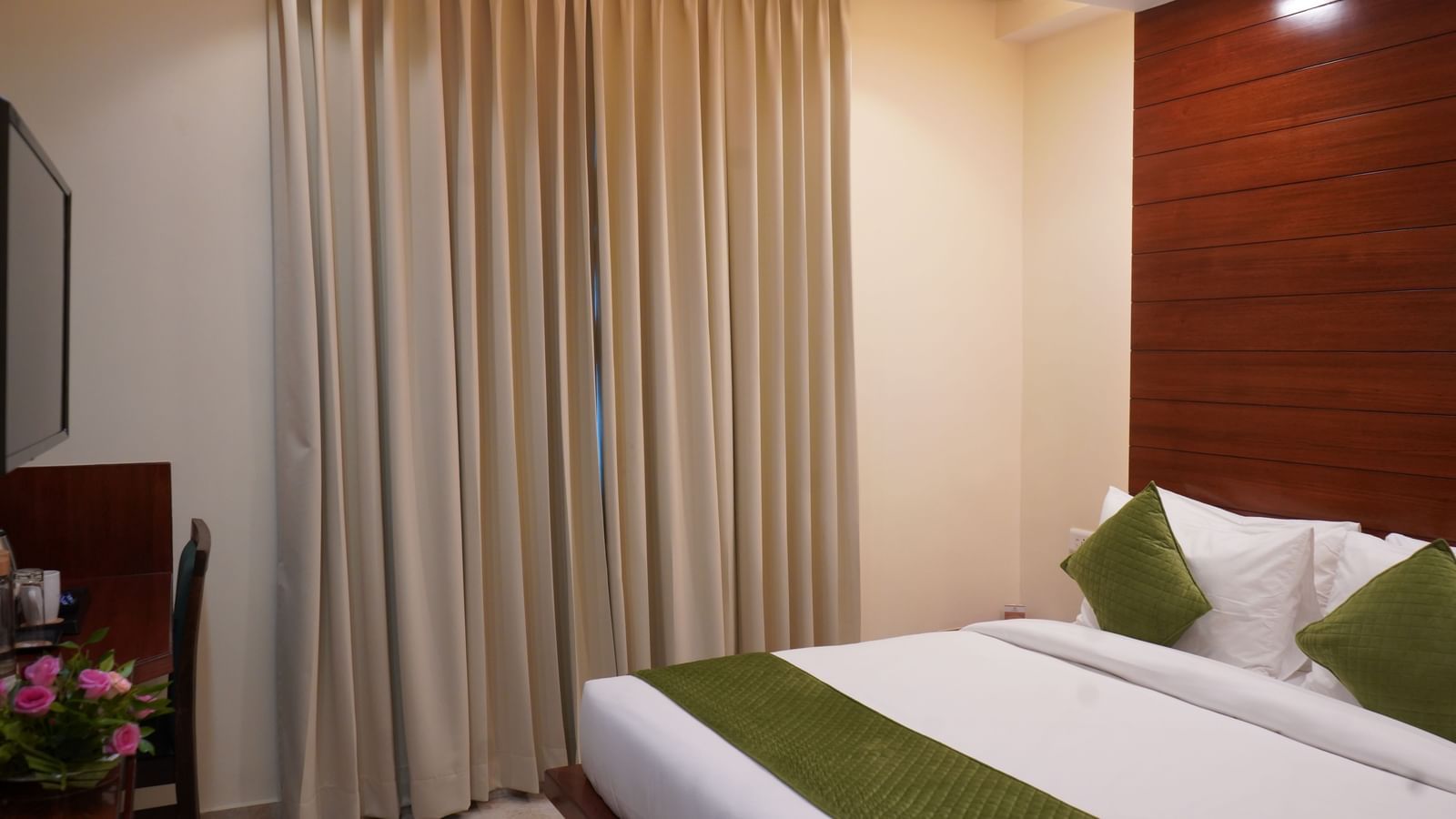 A wide shot of a hotel room bed with a white comforter and green accents. 