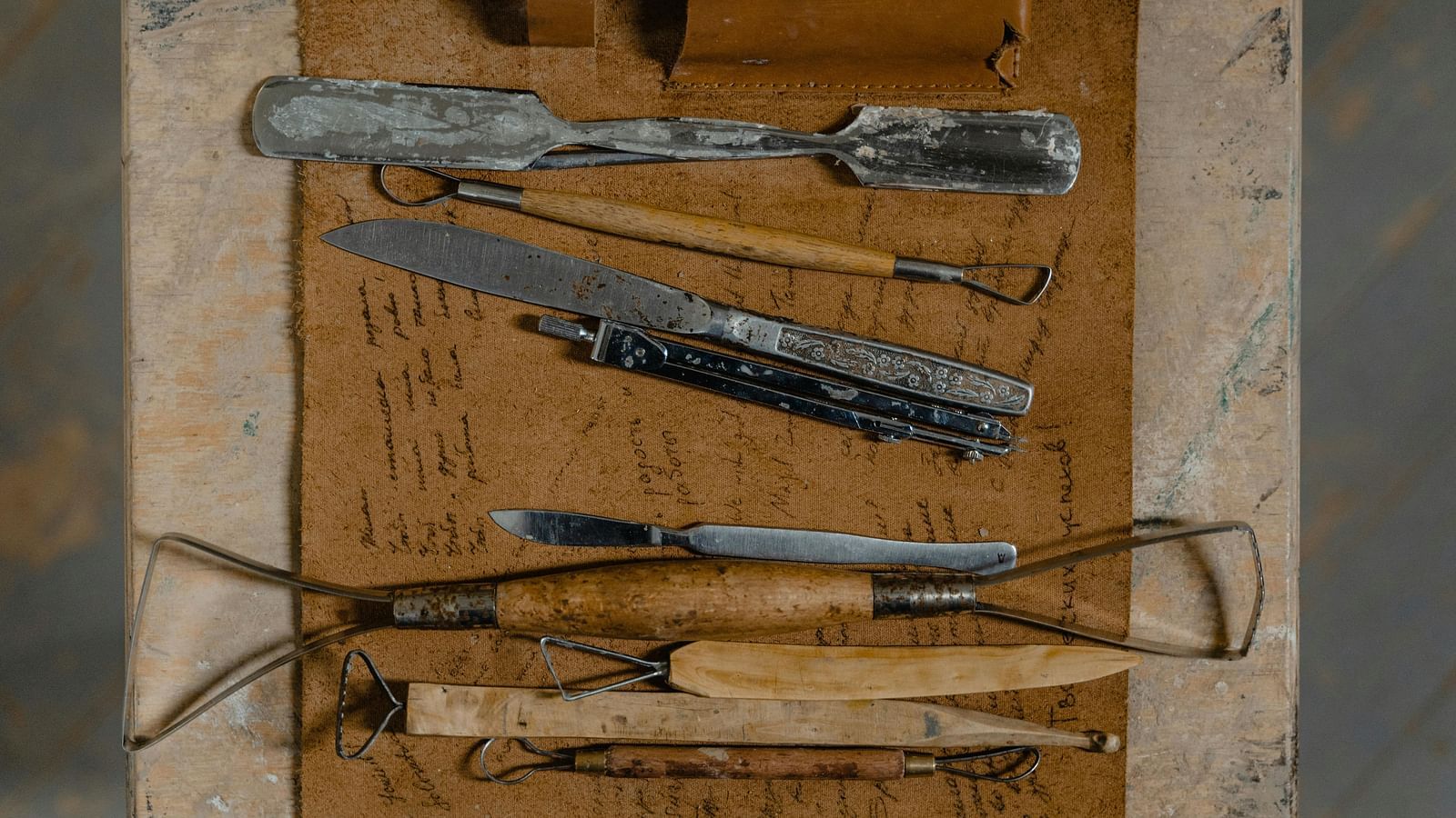 Assorted sculpting tools including chisels, hammers, rasps, and a Dremel tool arranged on a work surface.