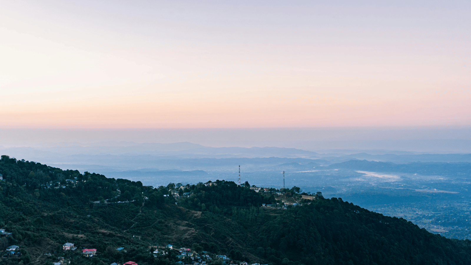 A panoramic view of a hillside town under a pastel coloured sky.