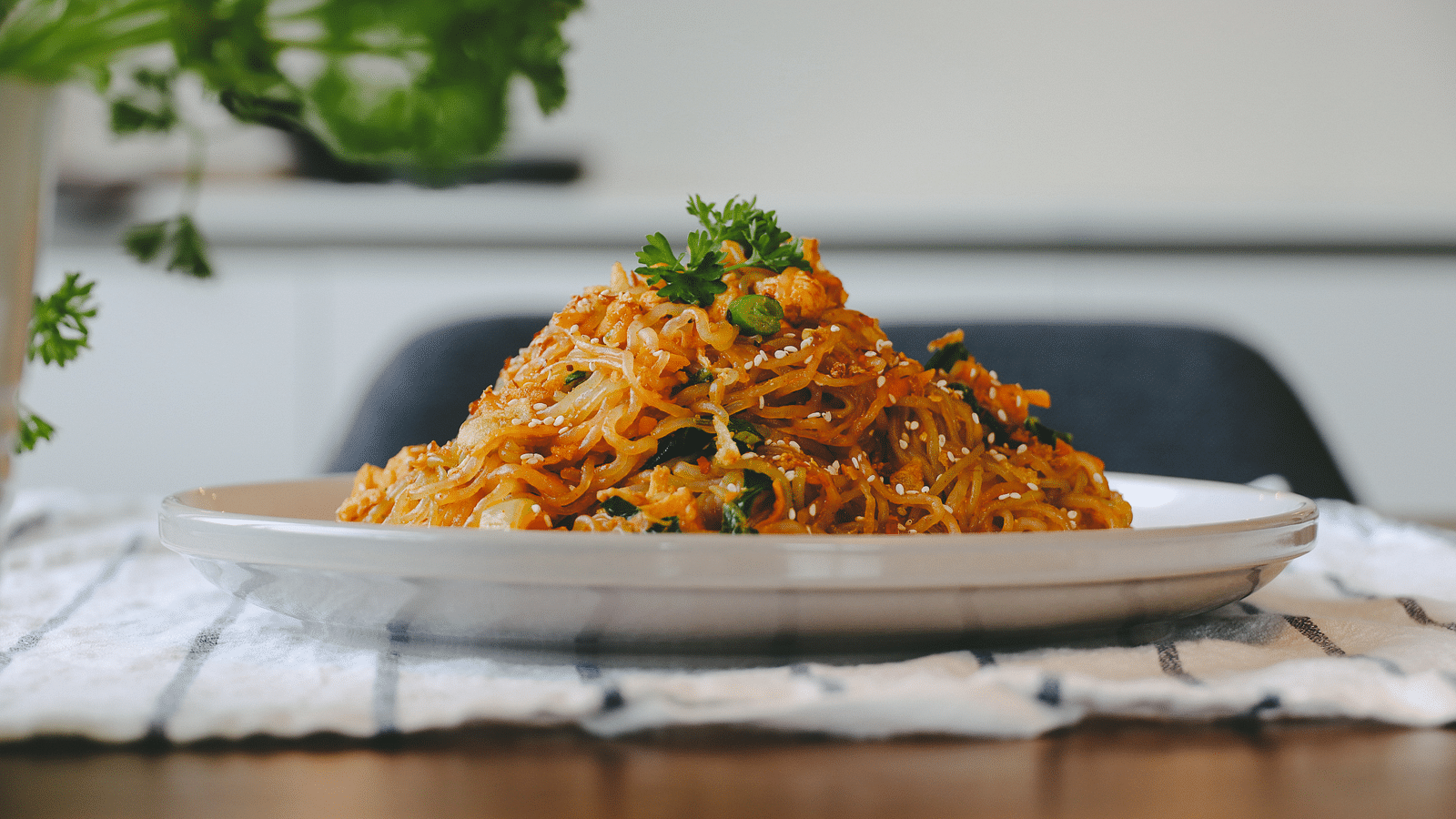 A plate consisting of Pad Thai placed on a table with a small plant in the background.
