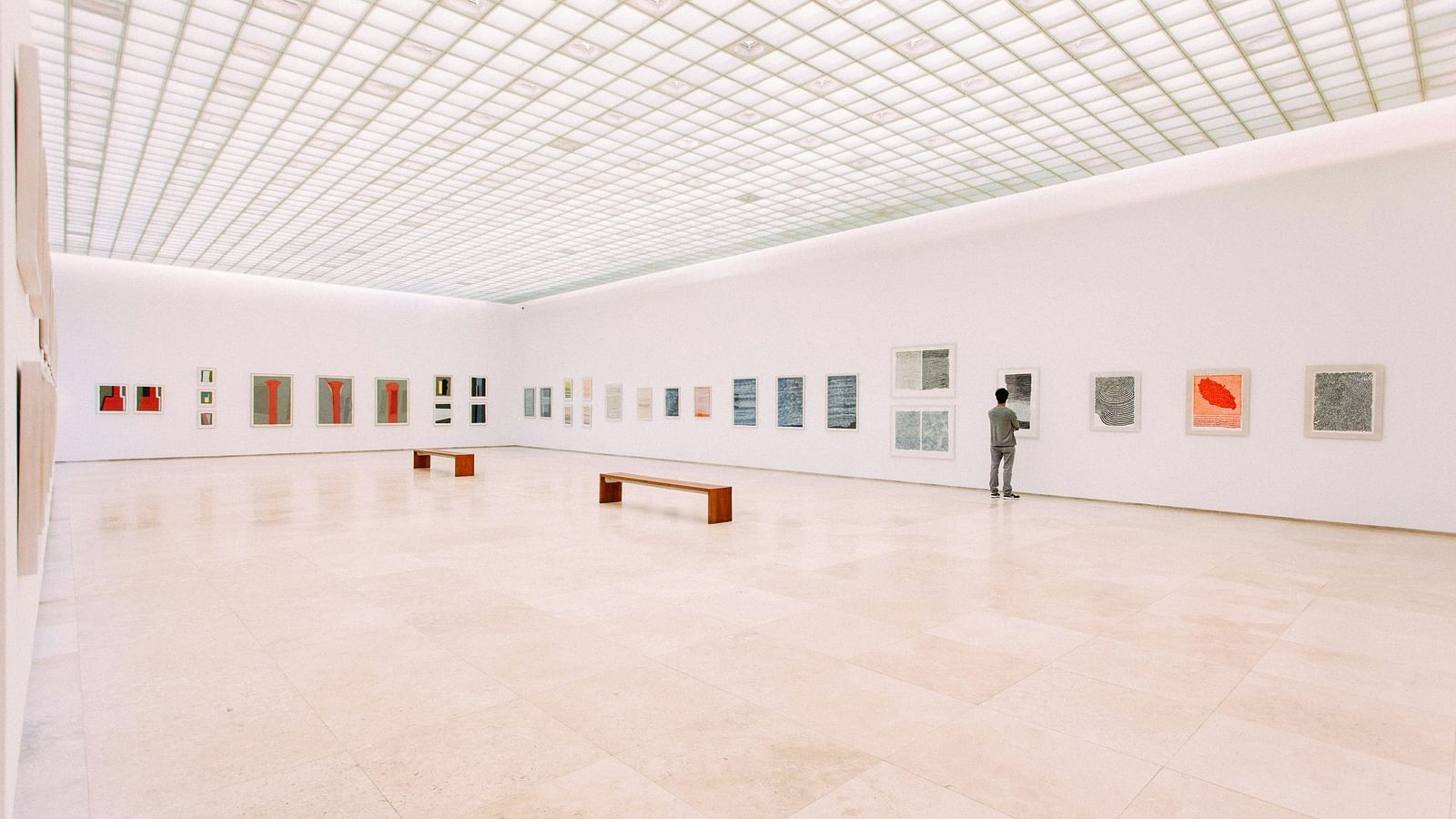 A solitary person looking at a painting in a museum that has painting across the wall.