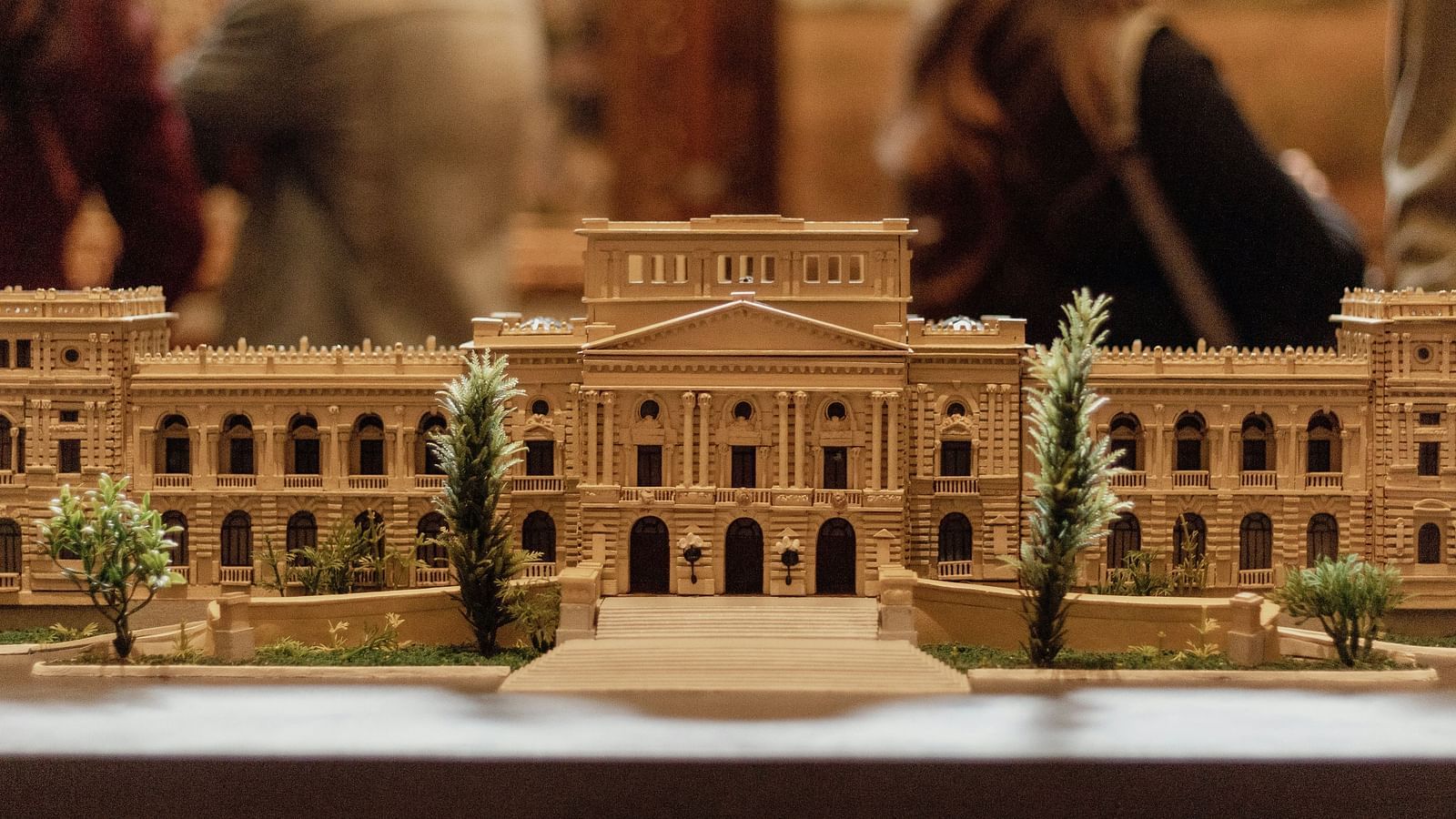 An overview of a miniature building inside a museum with artificial trees in front of it.