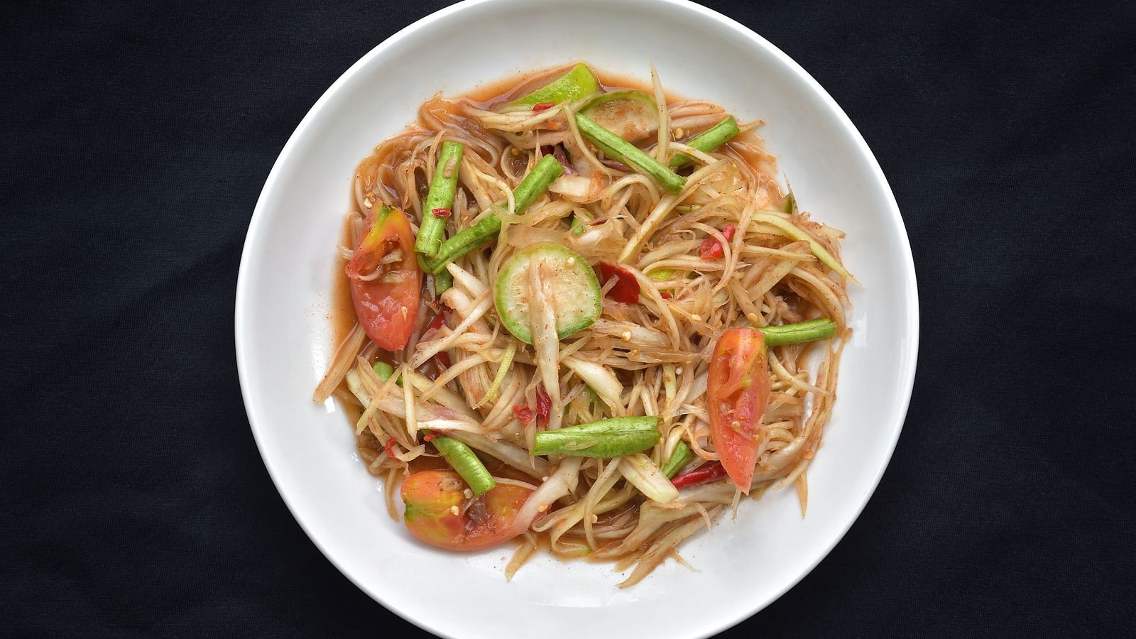 A top view of Som Tum (Papaya Salad) kept on a plate with a black background.