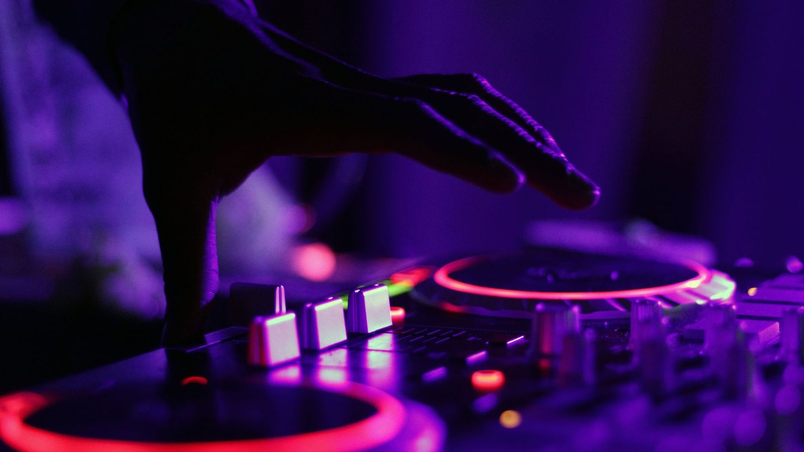 A close up shot of a person's hand on a DJ turn table that is lit up in neon colours.