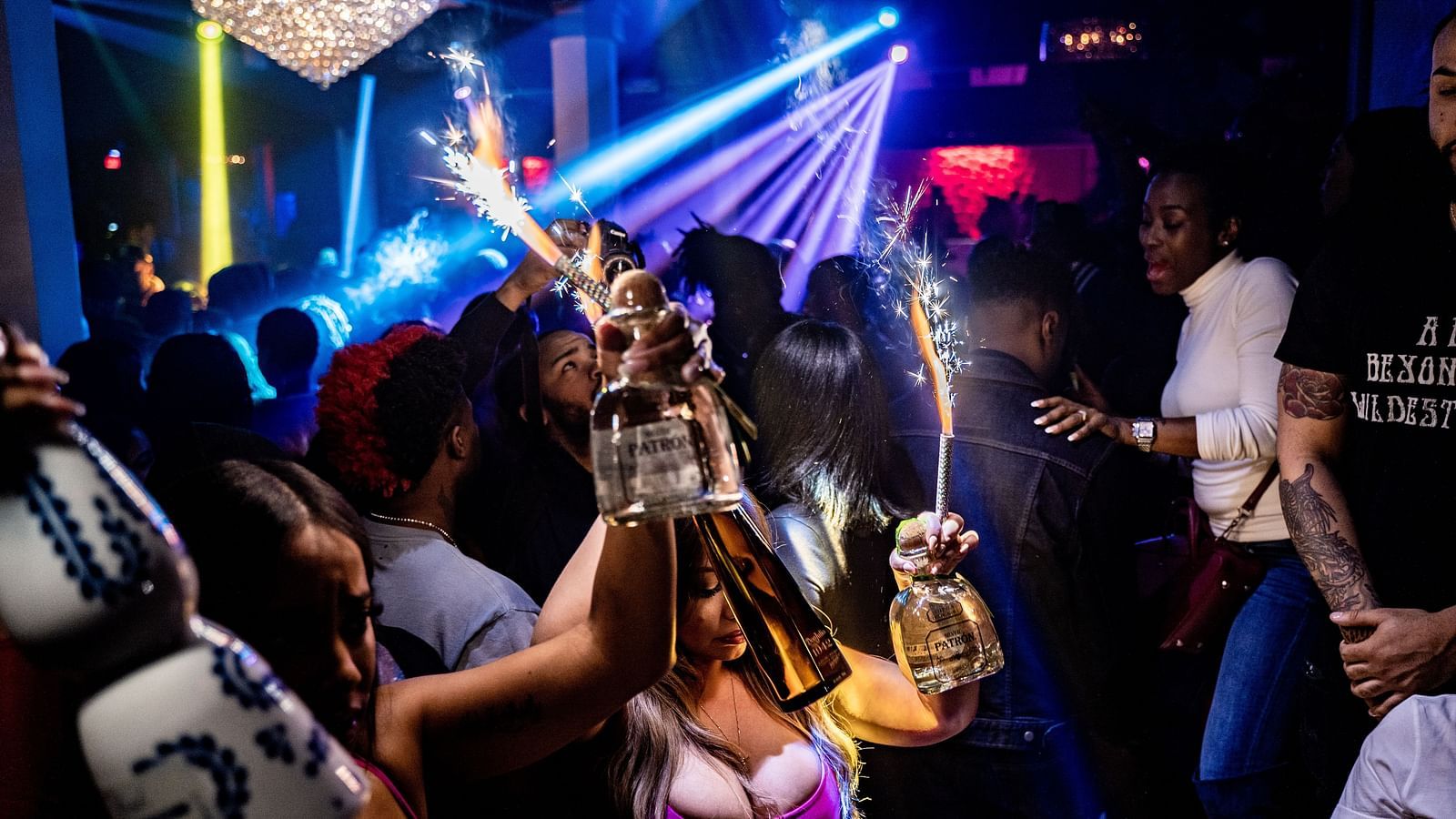 a group of people dancing in a club with waiters carrying bottles to give to the customers - 