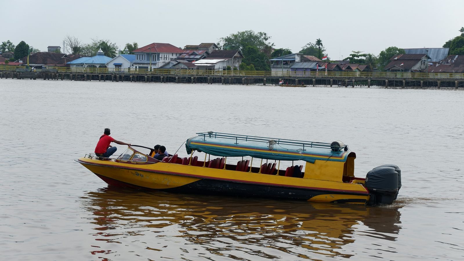 An overview of a passenger boat  with a person navigating it on a waterbody.