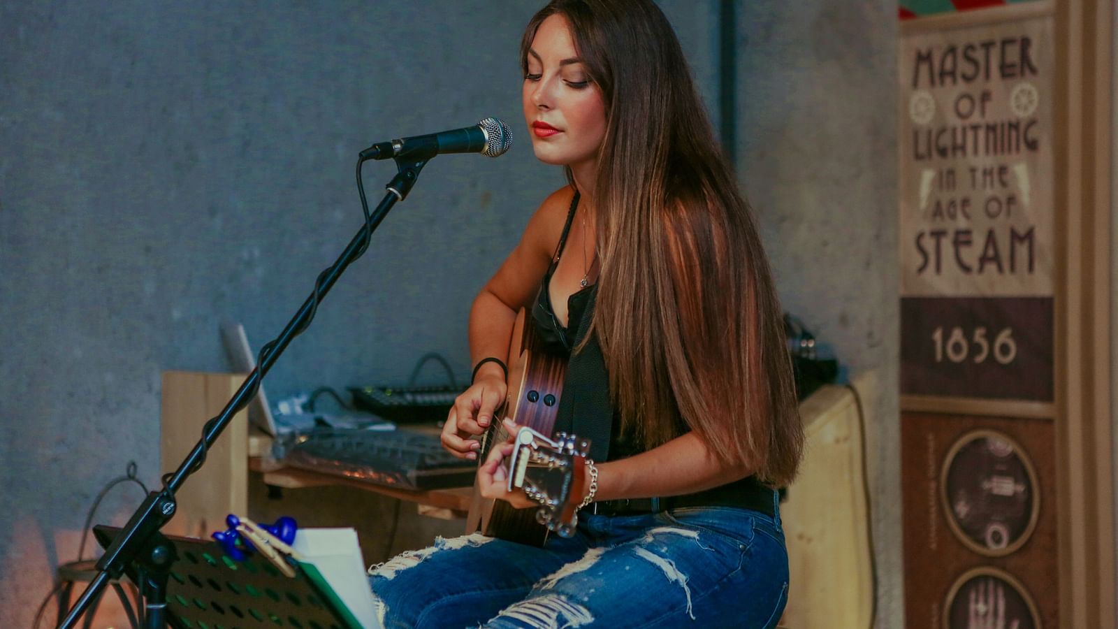 a woman sitting on a stool with a guitar and singing in a room
