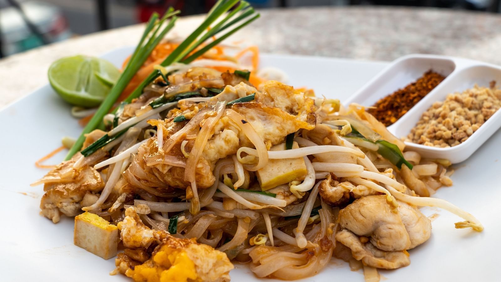 An overview of Pad Thai on a plate with sides, a slice of lime and garnishing on top.