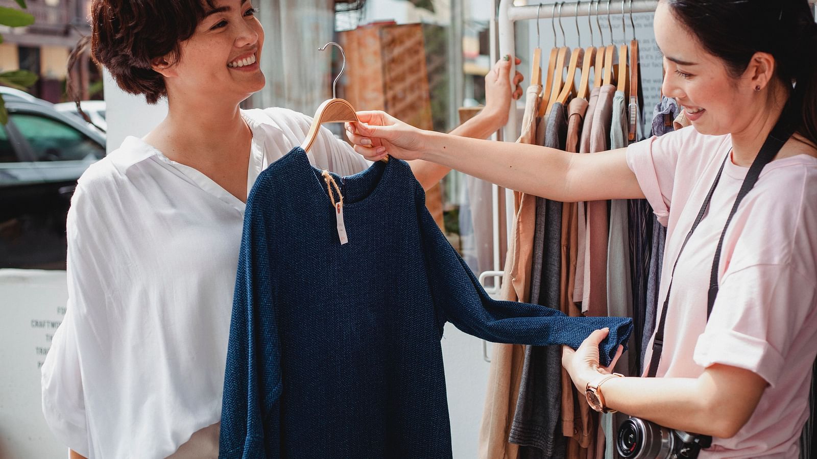 Two women shopping for clothes with one woman showing a top to another woman