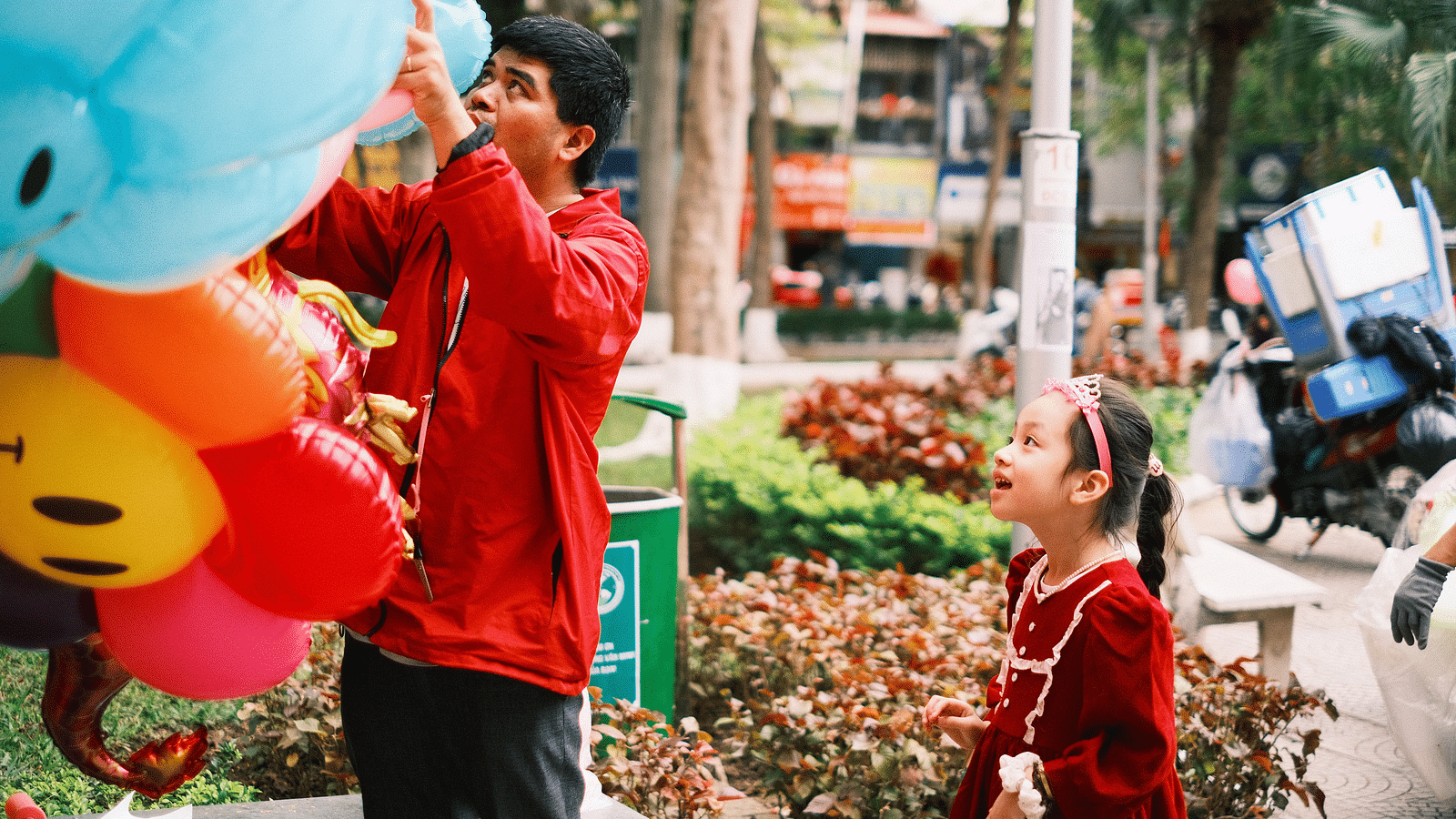 a girl looking at balloons while the balloon vendor is picking the balloon on the street