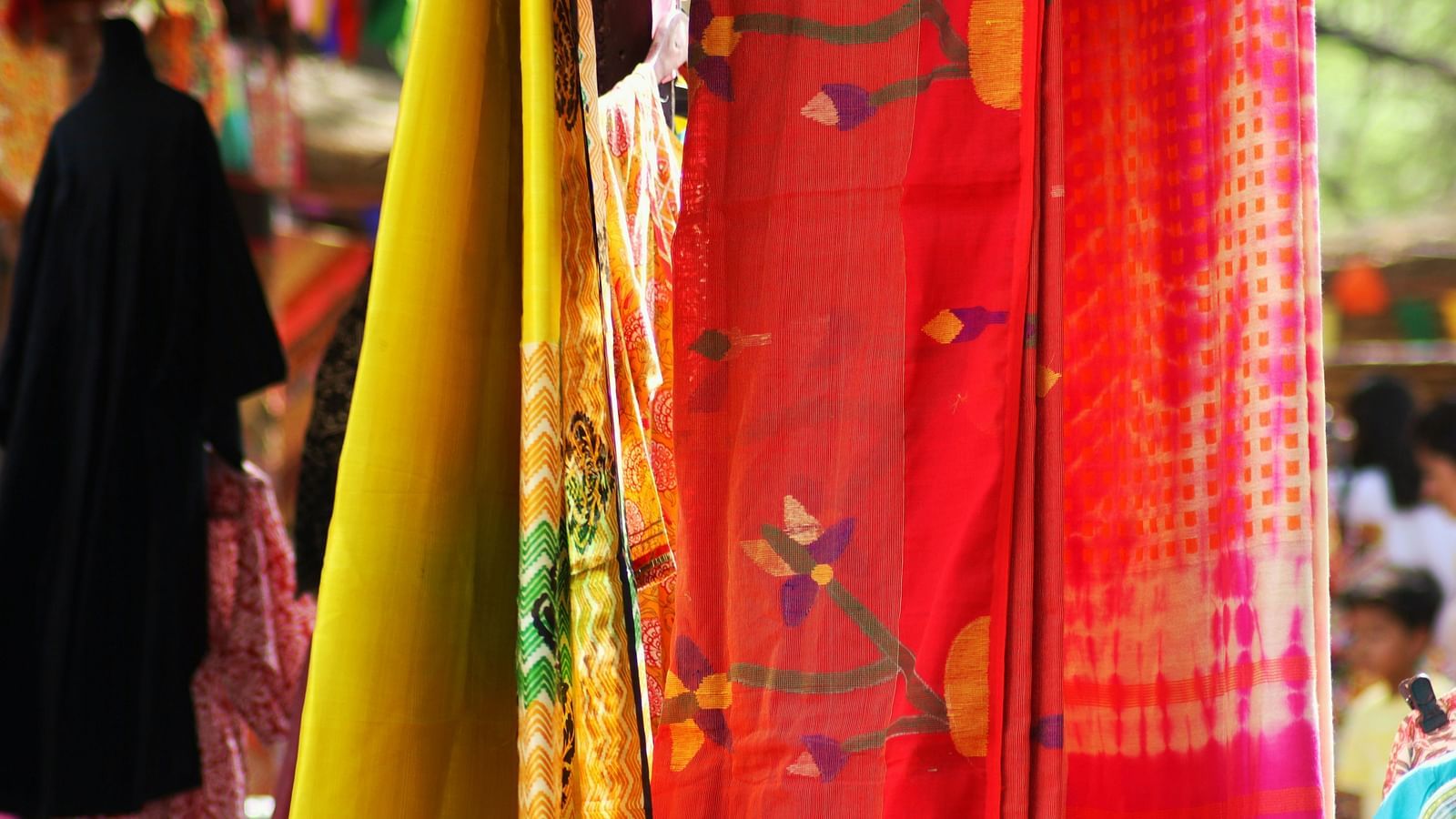 A close up of two silk clothes hung in an outdoor shop with people seen in the background.
